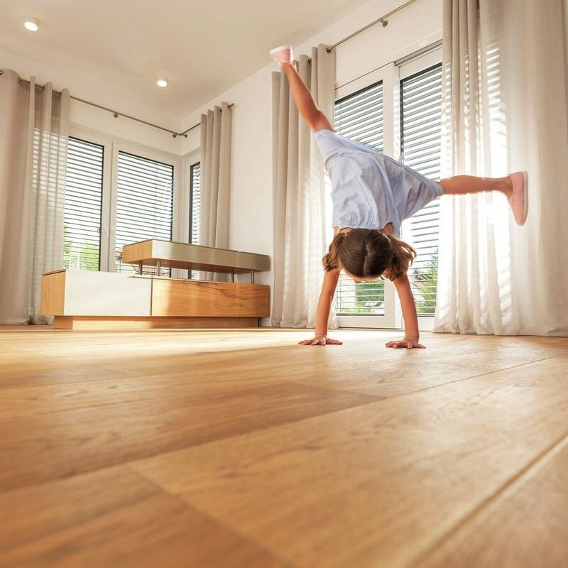 Ein junges Mädchen macht einen Handstand auf einem hochwertigen Parkettboden im Wohnzimmer.