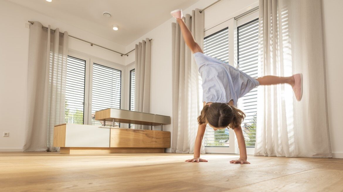 Ein junges Mädchen macht einen Handstand auf einem hochwertigen Parkettboden im Wohnzimmer.