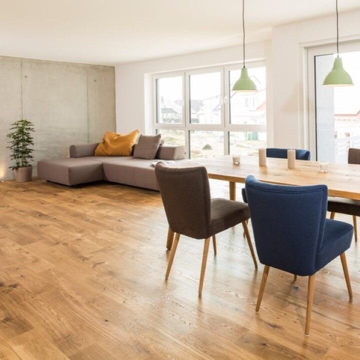 Moderner und Gemütlicher Wohnbereich mit Parkettboden. Im Vordergrund stehen Stühle und Esstisch. Im Hintergrund befindet sich ein Sofa.