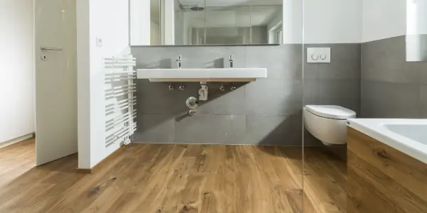 Parkettboden in einem Badezimmer. Es sind Teile der Badewanne, Toilette und einer Heizung zu sehen.