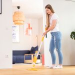 Eine junge Frau wischt den Parkettboden ihres Wohnzimmers mit dem Pallmann Spray Mop.