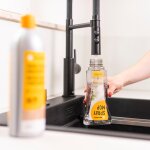 Der Nachfülltank des Spraymop Bodenwischers wird an einem schwarzen Wasserhahn mit Wasser aufgefüllt. Im Vordergrund steht eine Flasche Parkettreiniger, die unscharf zu erkennen ist.