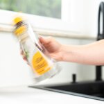 Der Flüssigkeitsbehälter des Sprühwischers wird von einer Person gut geschüttelt. In dem Behälter befindet sich das Wasser und das Reinigungsmittel. Durch die Schüttelbewegung erscheint das Gefäß leicht verschwommen.