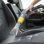 Anwendung des Kärcher Puzzi 10/1 Reinigungsgeräts auf einem Autositz. Die Nahaufnahme zeigt, wie das Handstück gehalten wird. Aus der Polsterdüse wird Reinigungsmittel auf den Sitz gesprüht.