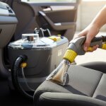Anwendungsbild des Kärcher Puzzi 10/1 Sprühextraktionsgeräts. Ein Autositz wird mit der Polsterdüse gereinigt. Der Schmutz wird von dem Gerät aus dem Sitz aufgesaugt. Die Autotür im Hintergrund ist geöffnet und der Waschsauger ist zu erkennen.